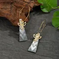 Detail of golden drop earrings with natural shell pendant on a grey textured fabric background - Gold Geometric Triangle Leaf Style (HWB256)