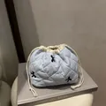 Light blue quilted drawstring makeup bag with black bow embroidery on a prop book - Blue
