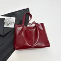 Deep red tote bag with leather texture and silver bow detail in a minimalist scene - Red