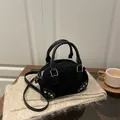 Borsa sottobraccio nera opaca con borchie argentate e tracolla su un tappeto accogliente - Nero