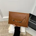 Bruine geweven envelop clutch met gouden metalen rand op een minimalistisch bureau - Bruin