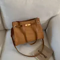 Sac cabas en daim marron avec boucle dorée posé sur un canapé en tissu blanc cassé - Marron