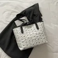 Pleated white tote bag with black bow prints and leather handles on a dark blazer - White