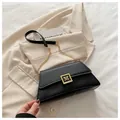 Elegante schwarze Pillow Bag mit goldenem M-Logo und Kettenriemen auf beigem Blazer - Schwarz