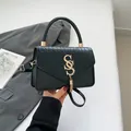 Black patchwork crossbody bag with gold S-logo and tassel detail on a minimalist background - Black
