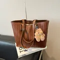 Brown woven leather tote bag with plush bear charm on white book and leather chair - With Pendant / Brown