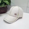Detail of white tweed baseball cap featuring a golden M logo and sparkling rhinestone trim - White