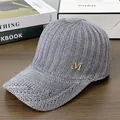 Silver knit baseball cap with gold crystal M logo displayed on a wooden surface - Adjustable / Gray