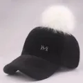 Detail der schwarzen Plüsch-Basecap mit weißem Kunstfell-Bommel und Metall M Logo - Erwachsene / Schwarzer Hut mit weißem Bommel