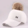 Detail of white plush baseball cap featuring a brown fur pom-pom and metal M letter - Adult / White Hat with Camel Pom Pom
