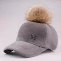 Detail of grey plush baseball cap with large faux fur pompom and metal M logo - Adult / Gray Hat with Camel Pom Pom