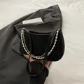 Elegante zwarte onderarmtas met parels en zilveren kettingen op een grijze blazer - Zwart