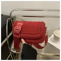 Dark red suede saddle bag with wide woven strap and golden hardware in lifestyle setting - Suede Red