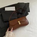 Chic brown retro leather underarm bag with gold oval buckle on a black blazer background - Brown