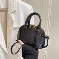Glossy black shell-shaped handbag with gold hardware and top handles shown with strap - Black without Pendant