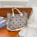 Grey corduroy tote bag with bow print and adjustable straps on a wooden bench - Gray