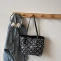 Minimalist black tote bag with white floral embroidery hanging on a wooden rack - Black