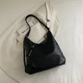 Borsa hobo minimalista in morbida pelle nera su sfondo di un completo beige chic - Stile di base / Nero