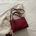 Elegante weinrote Lederhandtasche mit Goldaufschrift vor einem schicken Büro-Outfit - Rot