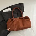 Borsa tote in camoscio marrone caramello con fibbia minimalista su sfondo di tessuto bianco - Marrone