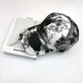 Dettaglio cappello da baseball tie-dye con strass e logo dorato appoggiato su libri - Adulto, Regolabile / Nero