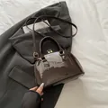 Borsa a conchiglia marrone scuro lucida con dettagli dorati e tracolla sottile inclusa - Marrone