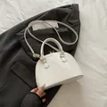 Borsa a conchiglia in vernice bianca con finiture dorate e manico su un blazer nero - Bianco
