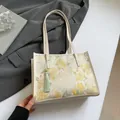 Chic beige floral brocade tote bag with green tassel on a modern grey blazer jacket - Yellow Floral Pattern
