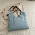 Light blue denim tote bag with brown rope shoulder straps and golden metal button accent - Light Blue