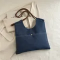 Blue denim tote bag with woven rope strap and gold button on plain blazer background - Blue