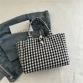 Gingham canvas tote bag with wooden toggle closure shown against a textured background - Black