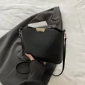 Minimalist matte black leather bucket bag with gold buckle on a dark grey blazer - Black