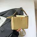Bolso bandolera dorado de cuero trenzado con logo V de metal sobre un traje gris - Dorado