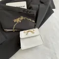 Mini borsa a sella bianca con fiocco dorato e tracolla a catena su blazer nero - Bianco