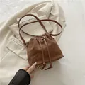 Bolso tipo cubo de ante marrón oscuro con cierre de cordón y detalles dorados elegantes - Marrón