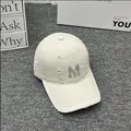 Detailed view of the rhinestone M logo and distressed fabric on a beige baseball cap - Adult One Size (Adjustable) / Beige