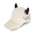 Dettaglio cappellino beige con corna nere, anelli metallici e spilla stile hip-hop - L (56-60cm) / Spilla da Balia Aereo Beige