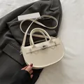 Elegante borsa a sella bianco avorio con chiusura a rotazione su blazer grigio - Bianco