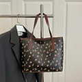 Retro black tote bag with red cherry print and brown leather straps on a hanger - Black