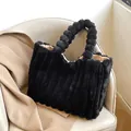 Black plush tote bag with vertical stripes and unique plush ball handles on leather chair - Black