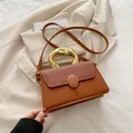 Braune Umhängetasche aus Leder mit Stoffklappe und goldenem Griff auf beige Sakko - Braun