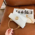 White mini handbag with woven flap and gold M logo on brown leather chair - White