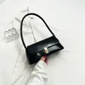 Glossy black French retro underarm bag with elegant gold buckle held by hand - Black