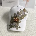 Vista macro di un cappello da baseball bianco con ricami floreali dorati e dettagli in strass - Bianco