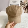 Detail of hand holding a brown linen newsboy cap against a vintage magazine background - L / Khaki