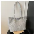 Borsa tote argento con trama a pieghe e rivetti dorati in un elegante ambiente studio - Grigio