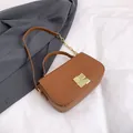Bolso bandolera cuadrado de cuero marrón con hebilla dorada y cadena sobre fondo de tela - Marrón