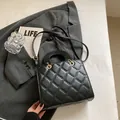 Bolso bandolera acolchado negro con detalles dorados y asa sobre una chaqueta gris - Negro
