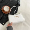 Bolso baguette blanco con textura de cocodrilo y lazo dorado en una mesa de café - Blanco