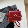 Bolso bandolera rojo oscuro con lazo dorado y costuras de chevrón en cuero mate - Rojo